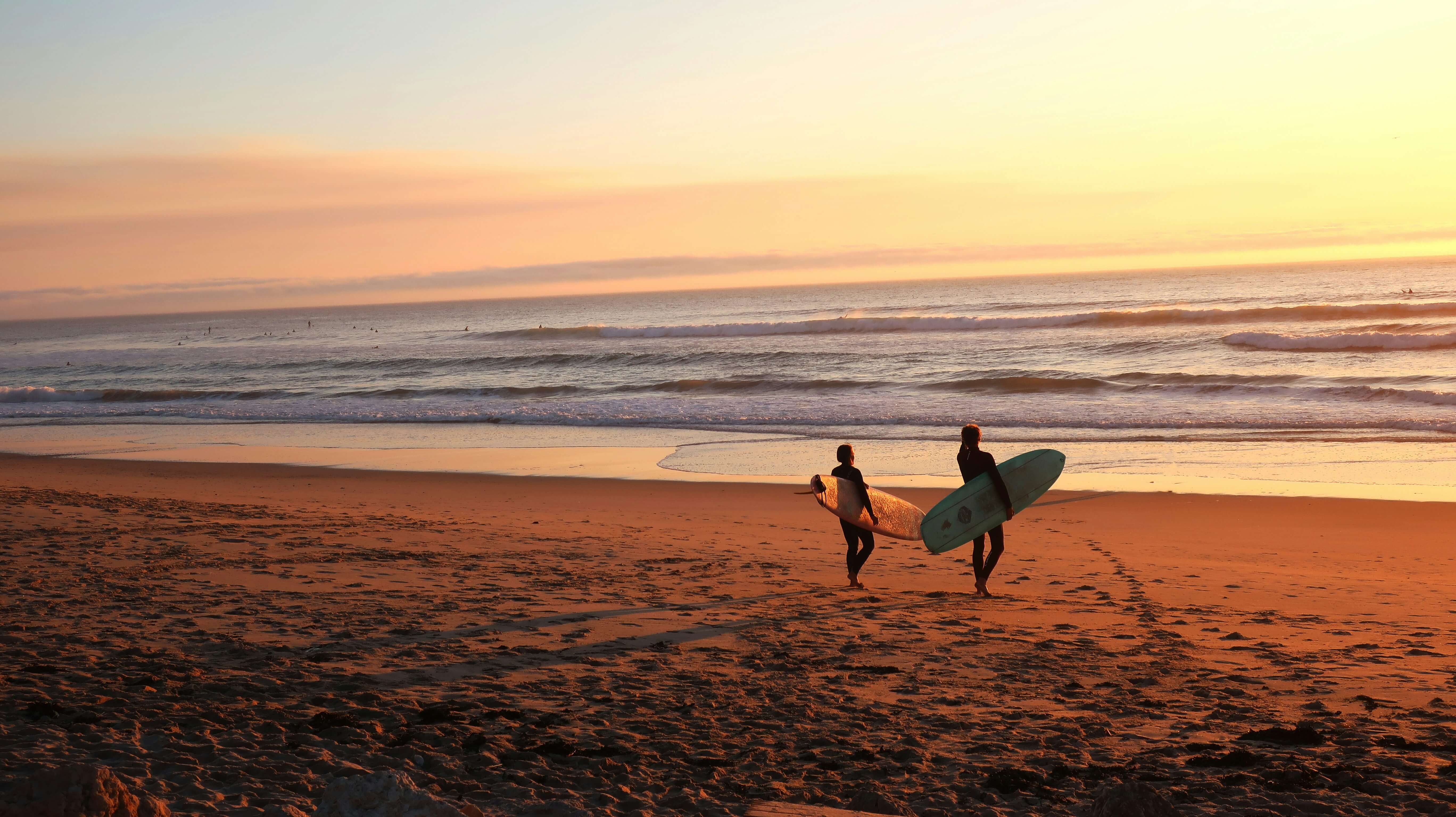 two surfers walking towards the water after reading a surf report