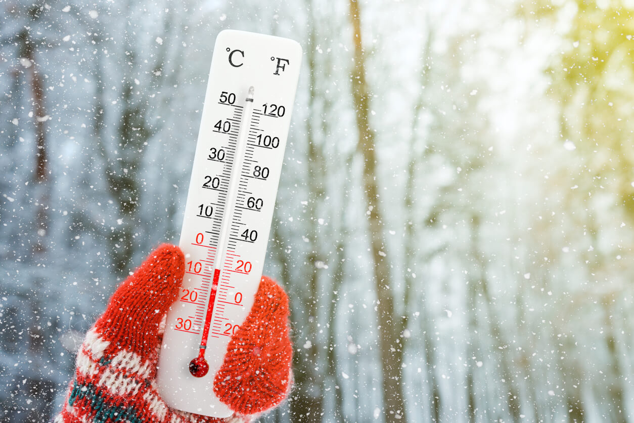 a mitten holding a thermometer in a snowy environment that's reading the temperature but not the feels like temperature